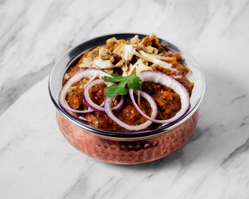 Delhi Darbar curry in a copper bowl, topped with onions, ginger and cilantro